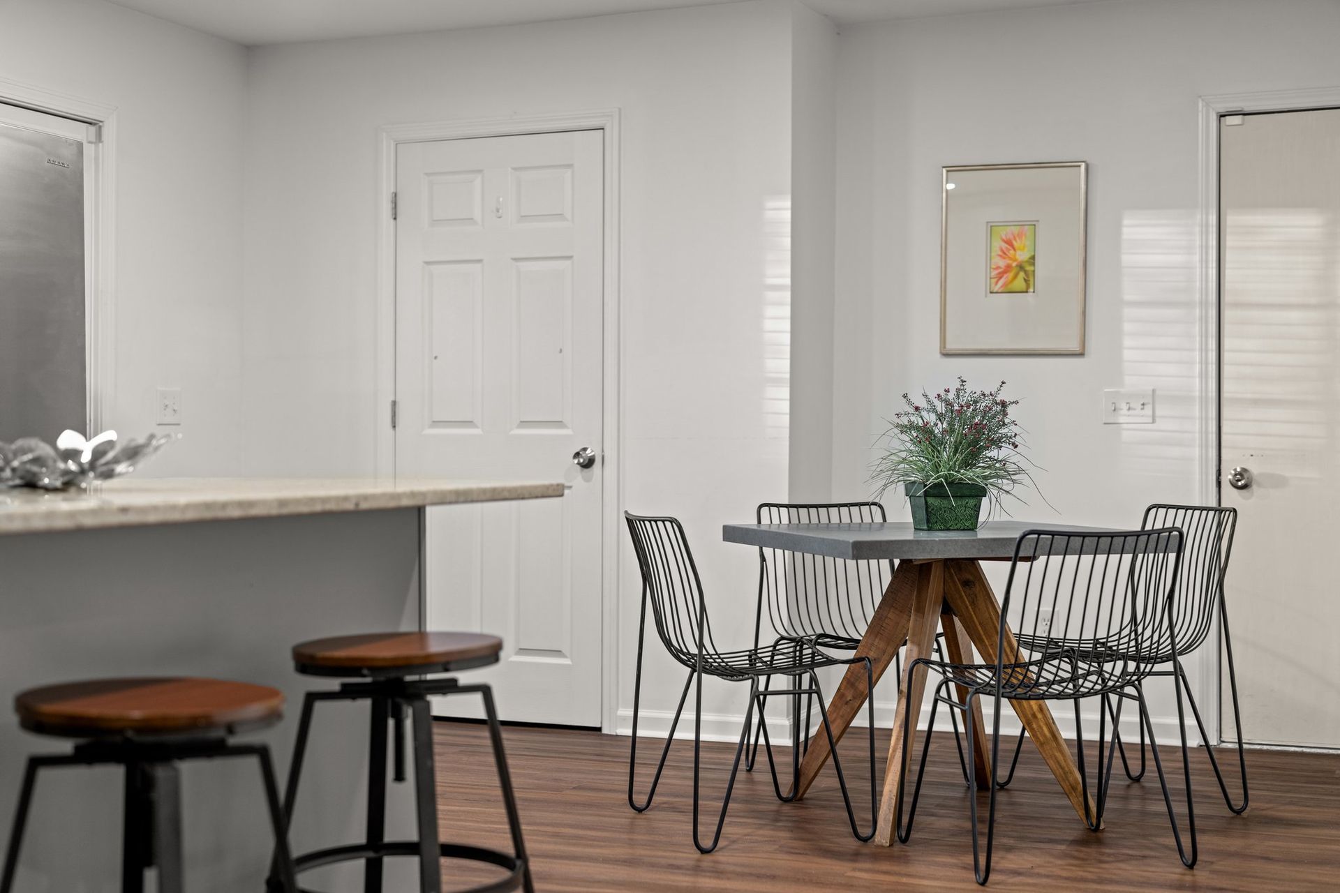 Modern dining area with wire chairs, round table, wooden floor, and a kitchen counter with stools