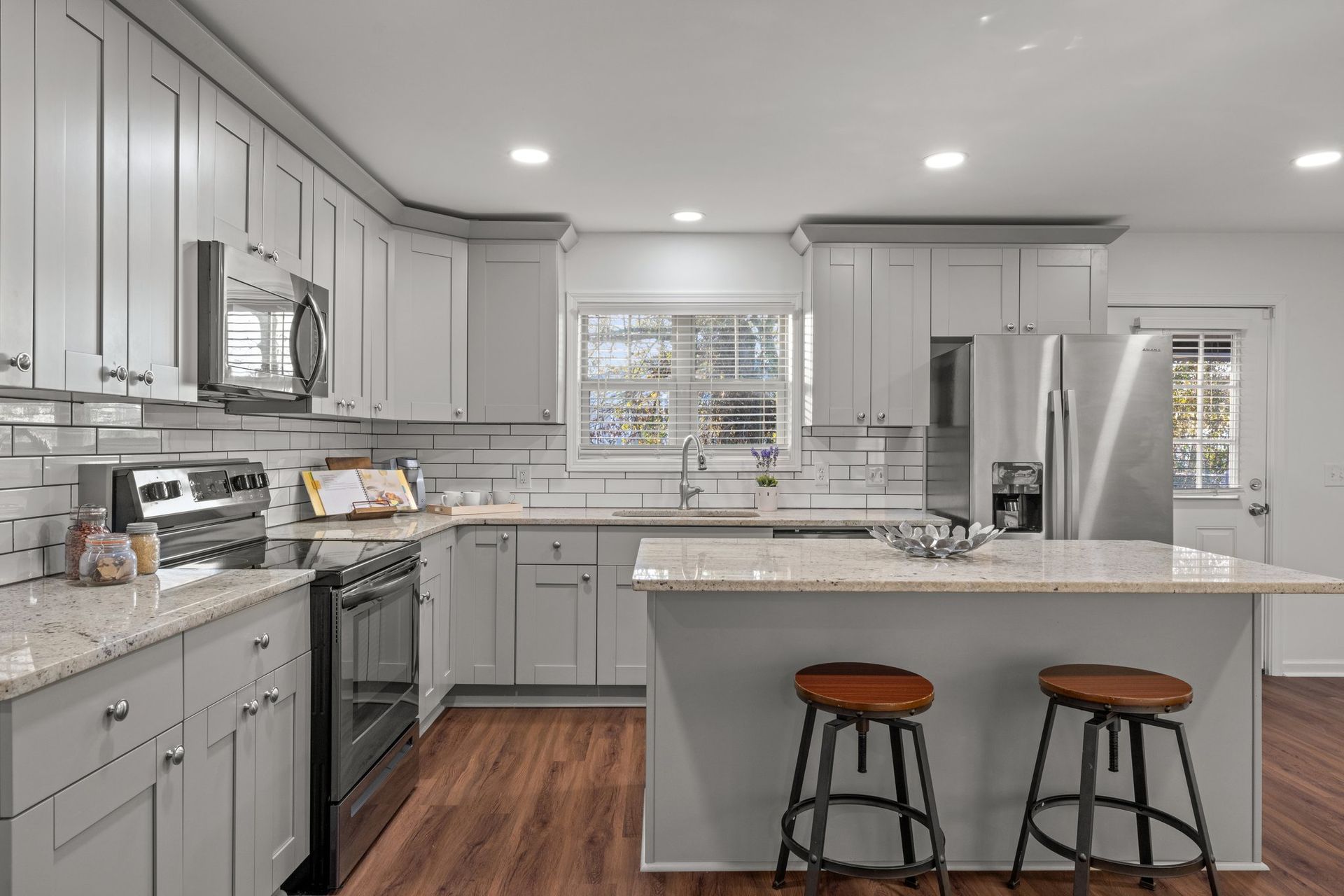 Bright modern kitchen with gray cabinets, white countertops, stainless steel appliances, and two stools at the island