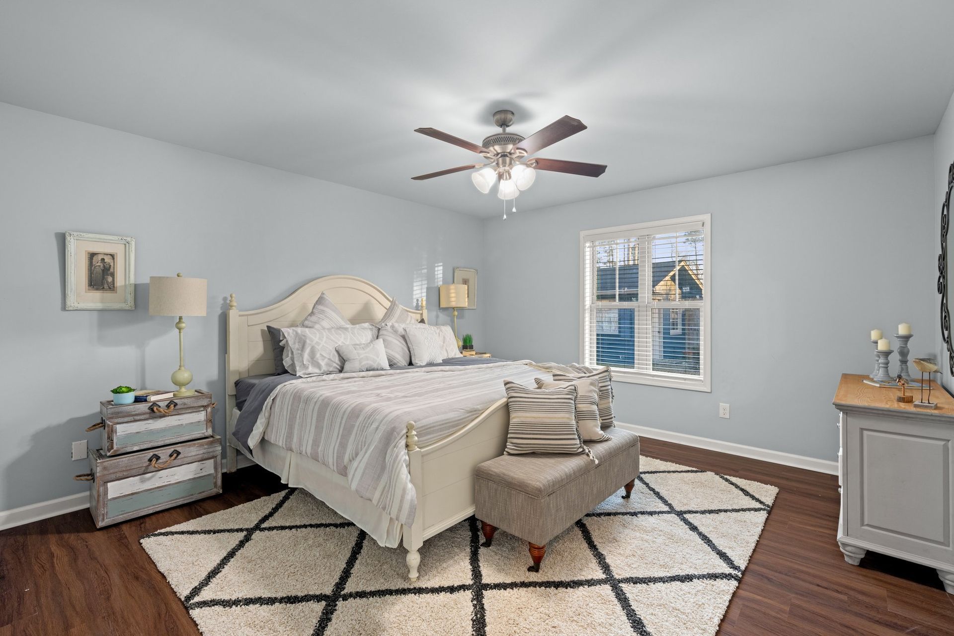 Bright bedroom with a white bed, patterned rug, gray walls, and a window letting in daylight.