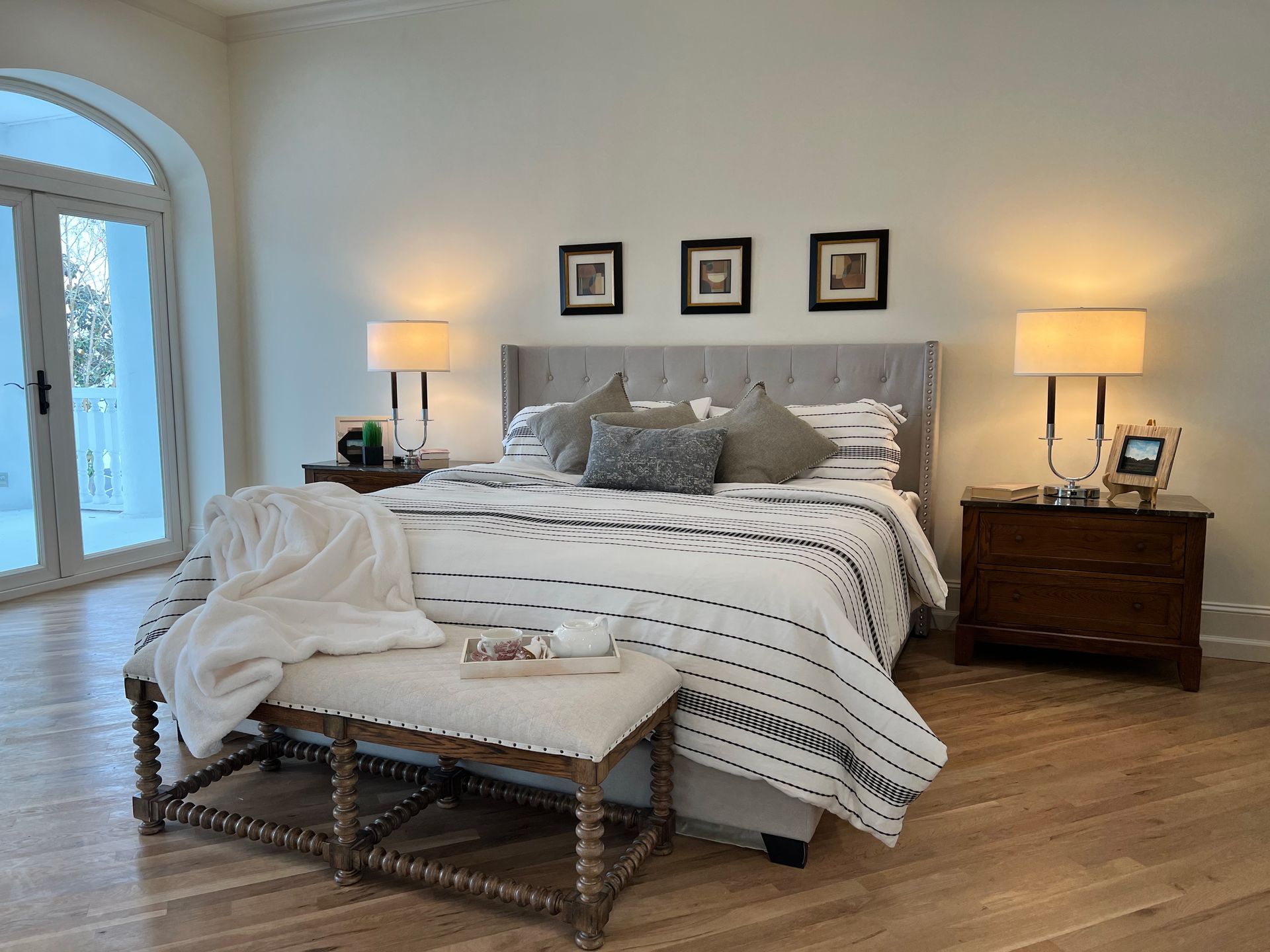 Bright bedroom with a white bed, striped bedding, bedside lamps, and a large window.