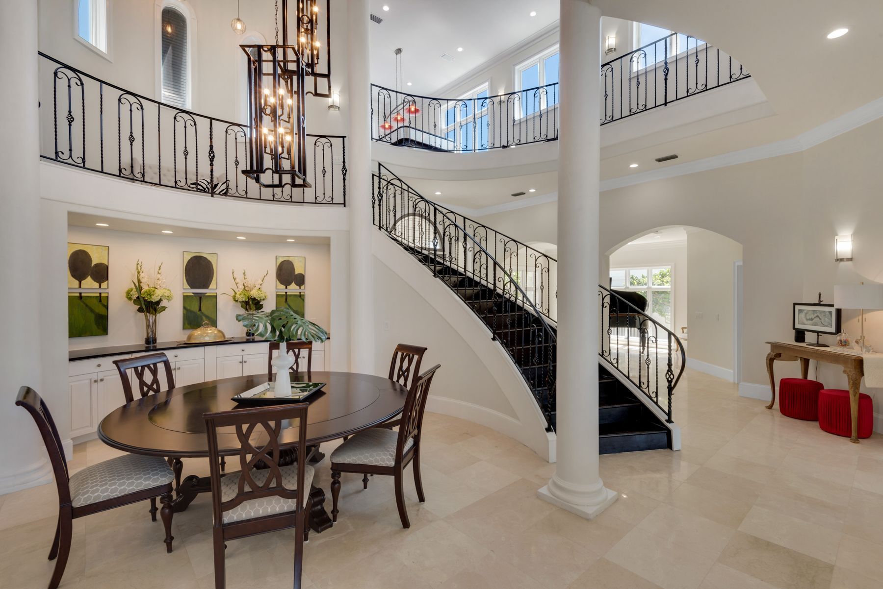 Spacious foyer with curved staircase, chandelier, round table, and bright white walls and columns