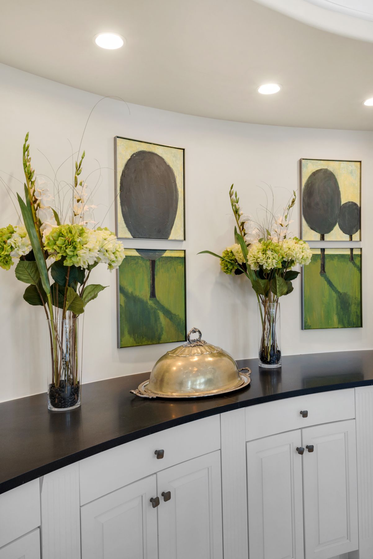 Decorative console table with flowers, framed art, and a silver serving dome in a bright hallway