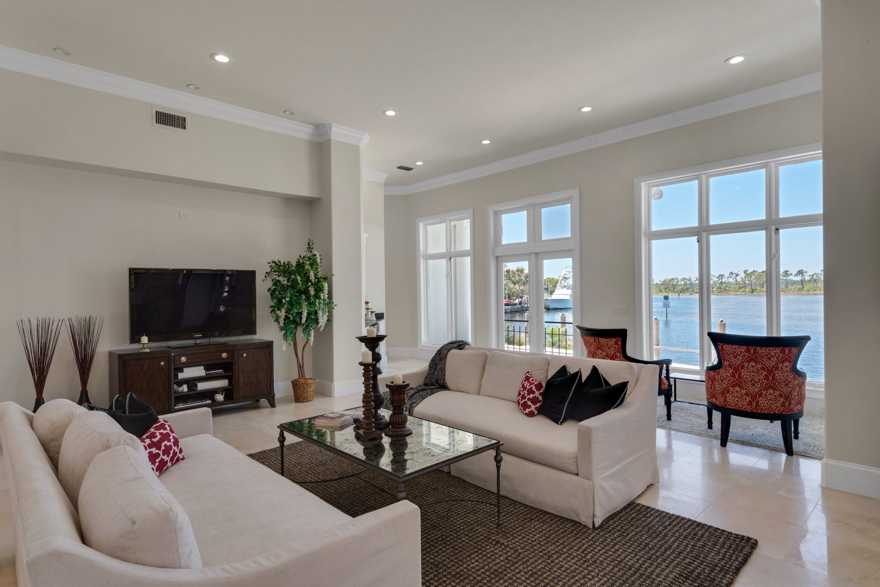 Bright modern living room with white sofas, TV, dining nook, and large windows overlooking water