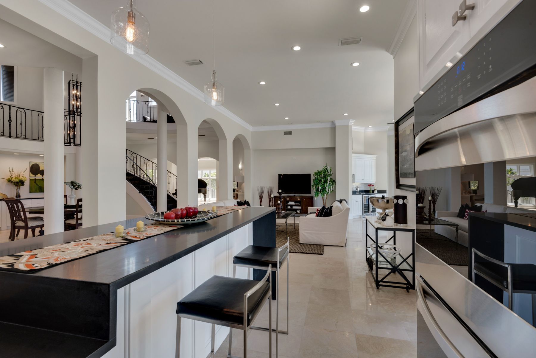 Bright modern kitchen with a long black island, white cabinets, bar stools, and arched openings into a living area