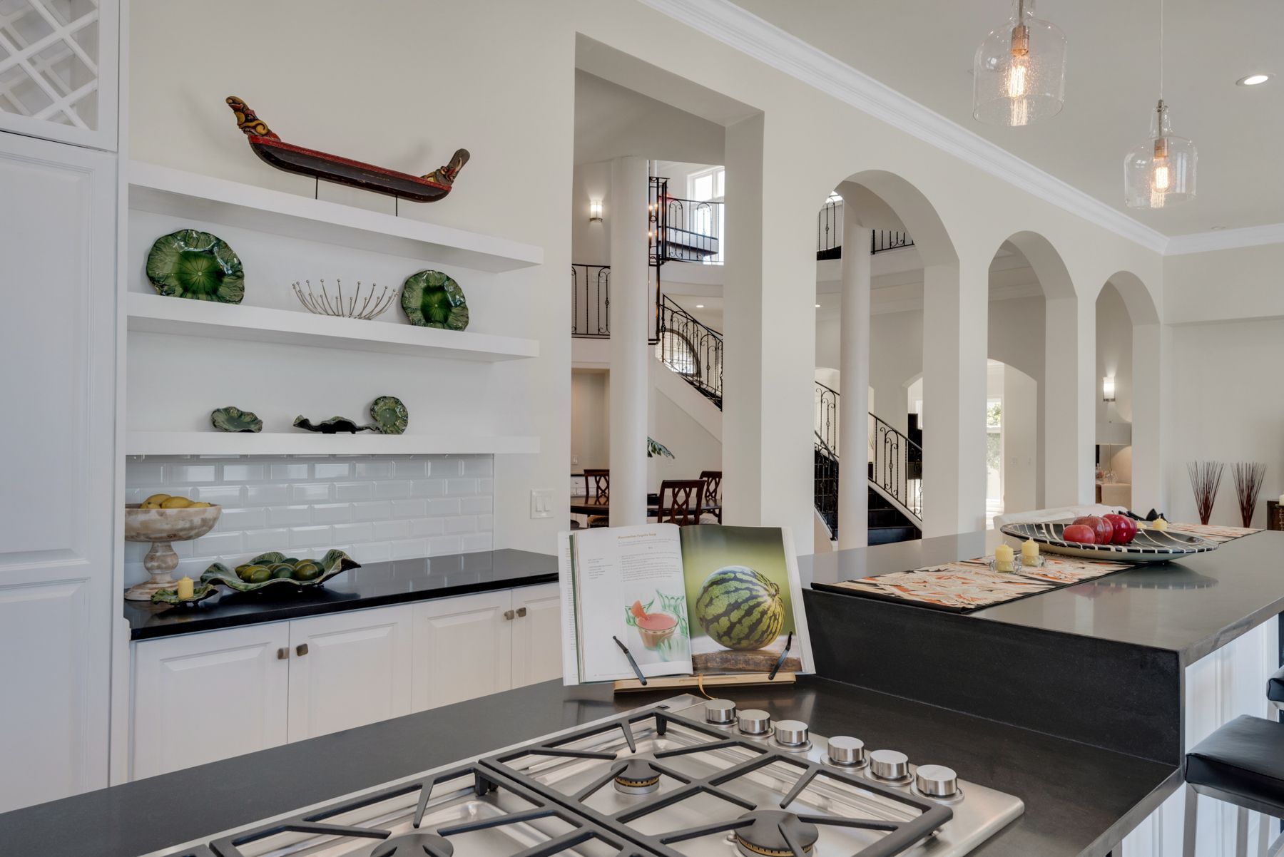 Modern kitchen with white shelves, black island, and arched doorways in a bright open interior