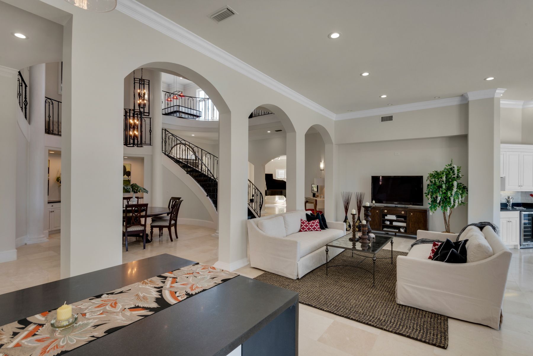 Spacious modern living room with white sectional sofas, staircase, arched doorway, and high ceilings