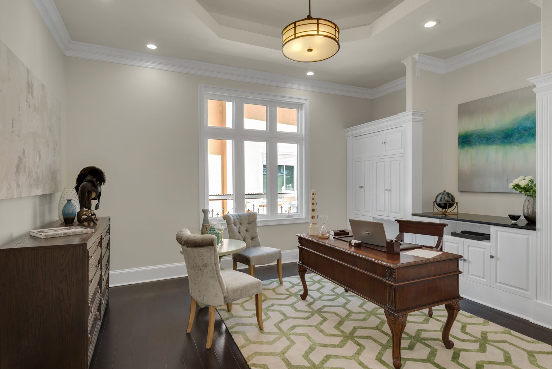 Bright home office with a desk, chair, window, and patterned rug in a white room.