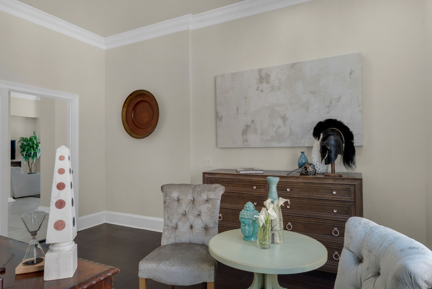 Bright living room with gray chairs, round table, dresser, wall art, and decorative accents.