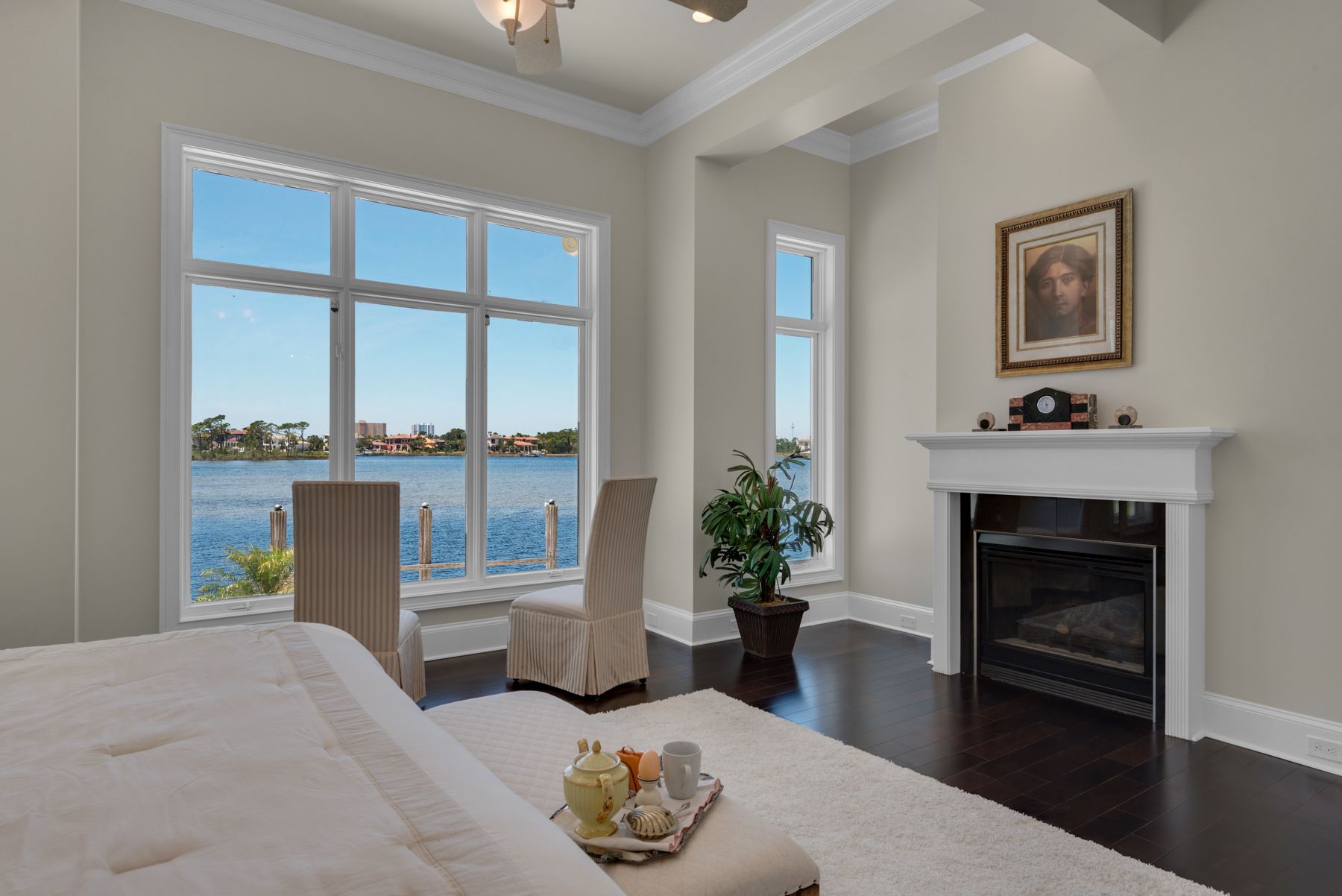 Bright bedroom with water view, fireplace, and a window seat in neutral tones.