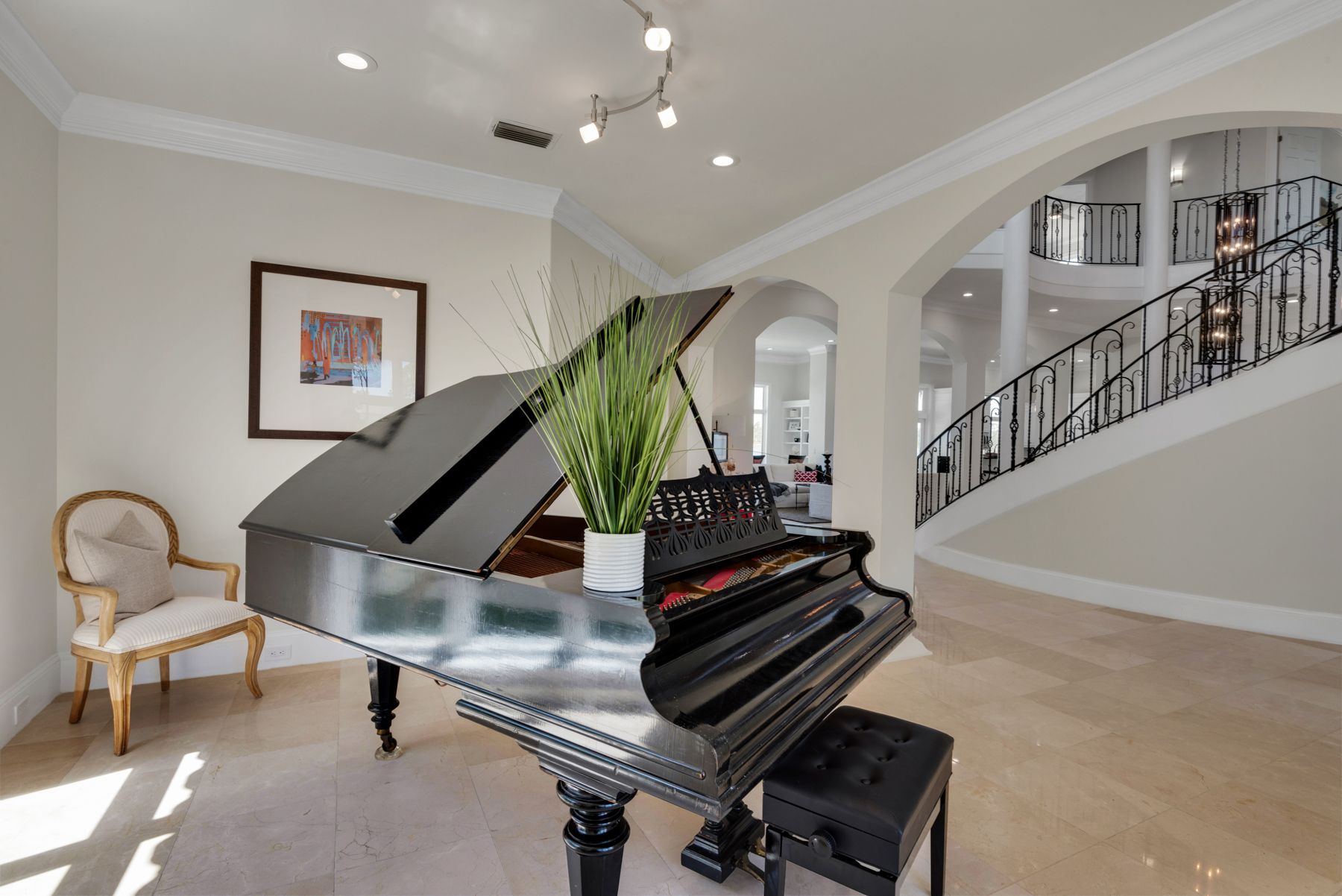 Grand piano in a bright living room with arched entryways and a staircase in the background