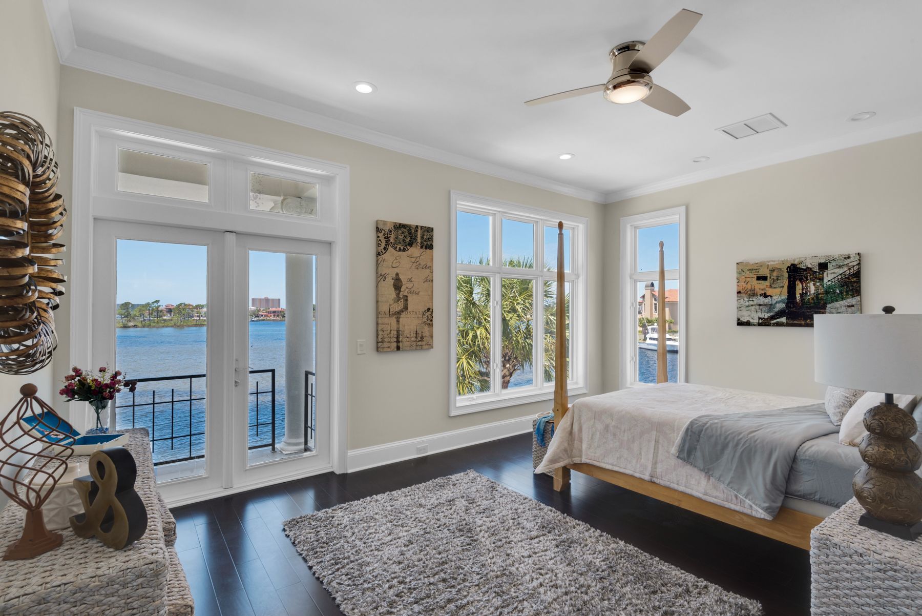 Bright bedroom with ocean-view windows, white decor, gray bed, and ceiling fan