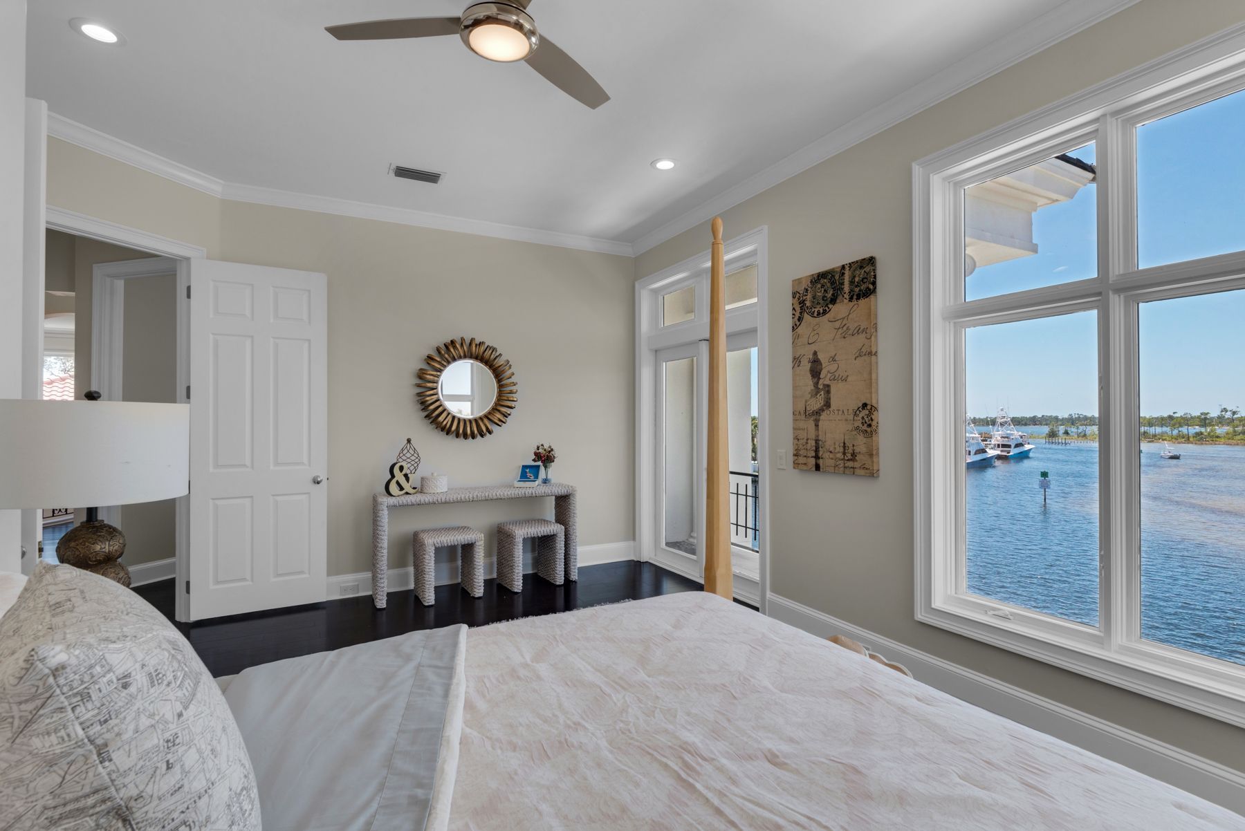 Bright bedroom with a bed, fireplace, ceiling fan, and large windows overlooking water