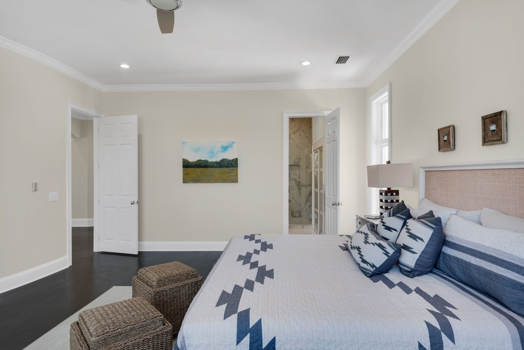 Bright bedroom with a large bed, blue accents, beige walls, and a landscape painting near an open door.