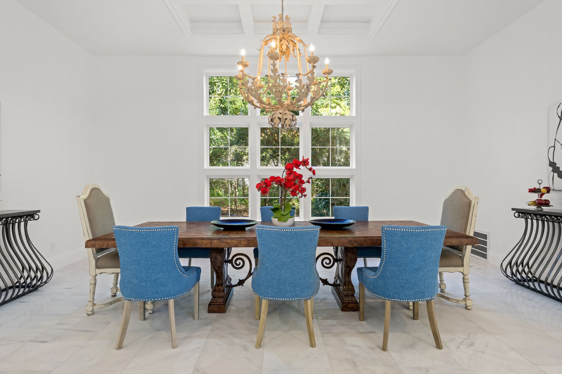 Elegant dining room with blue chairs, wooden table, chandelier, and a floral centerpiece by bright windows