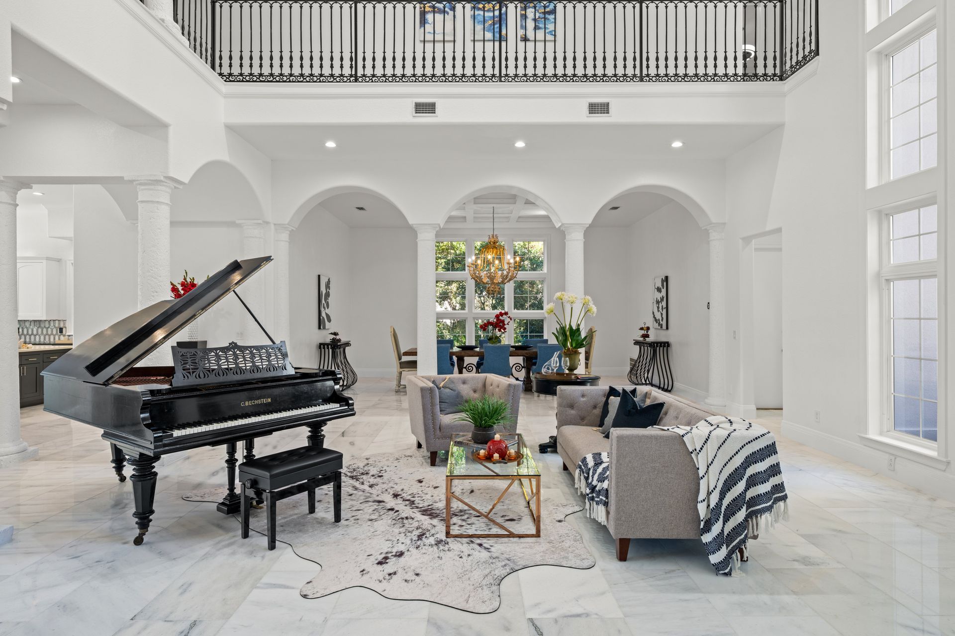 Bright white living room with grand piano, gray sofas, large windows, and floral decor
