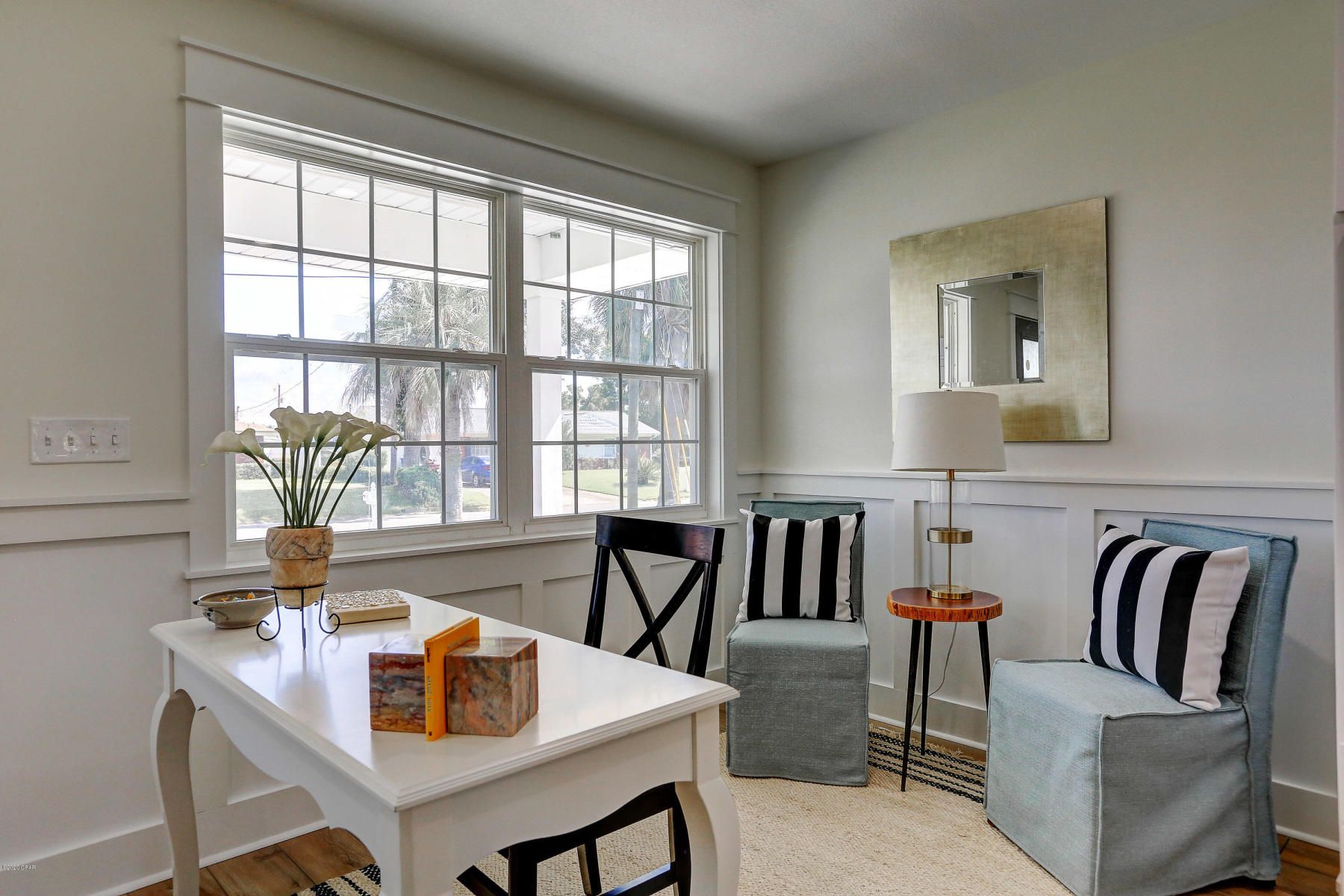 Bright dining nook with white table, black chairs, striped armchairs, lamp, mirror, and large window