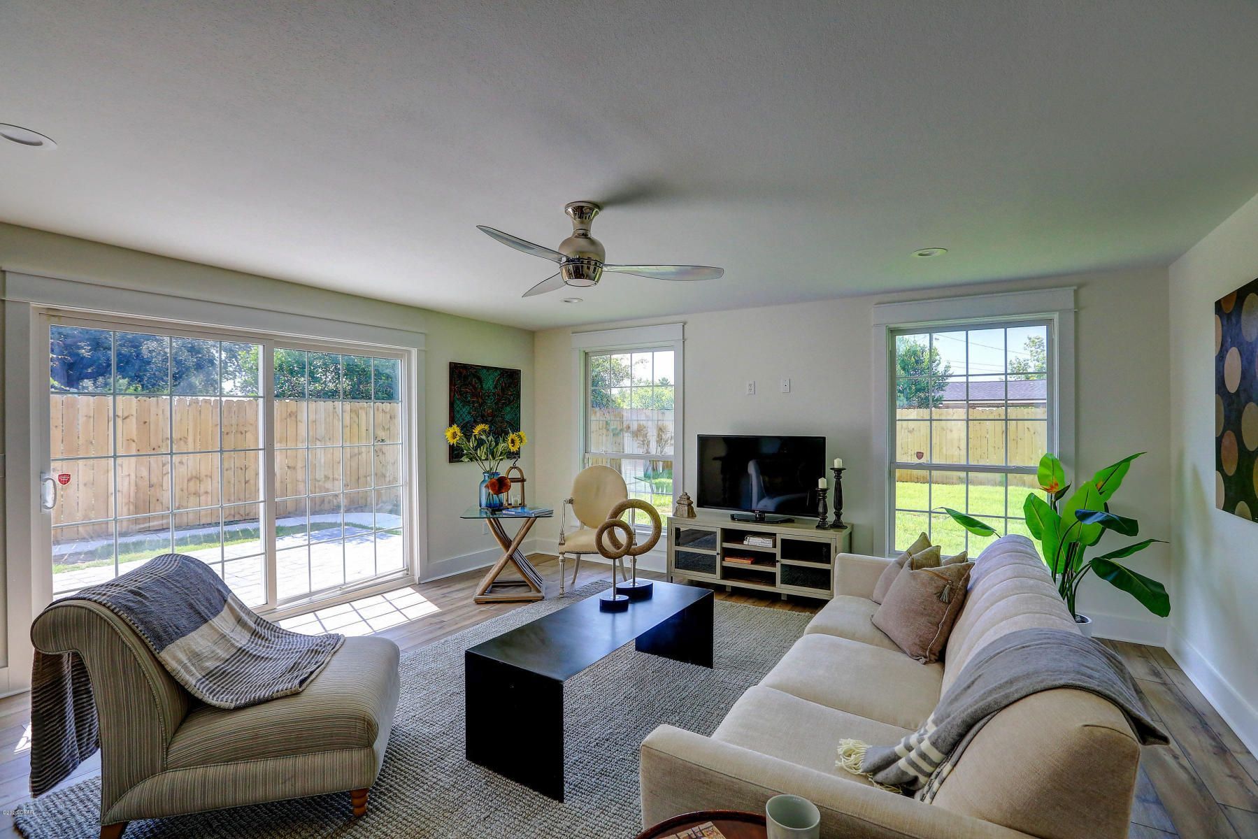 Bright living room with large windows, beige sofa, black coffee table, TV, and ceiling fan