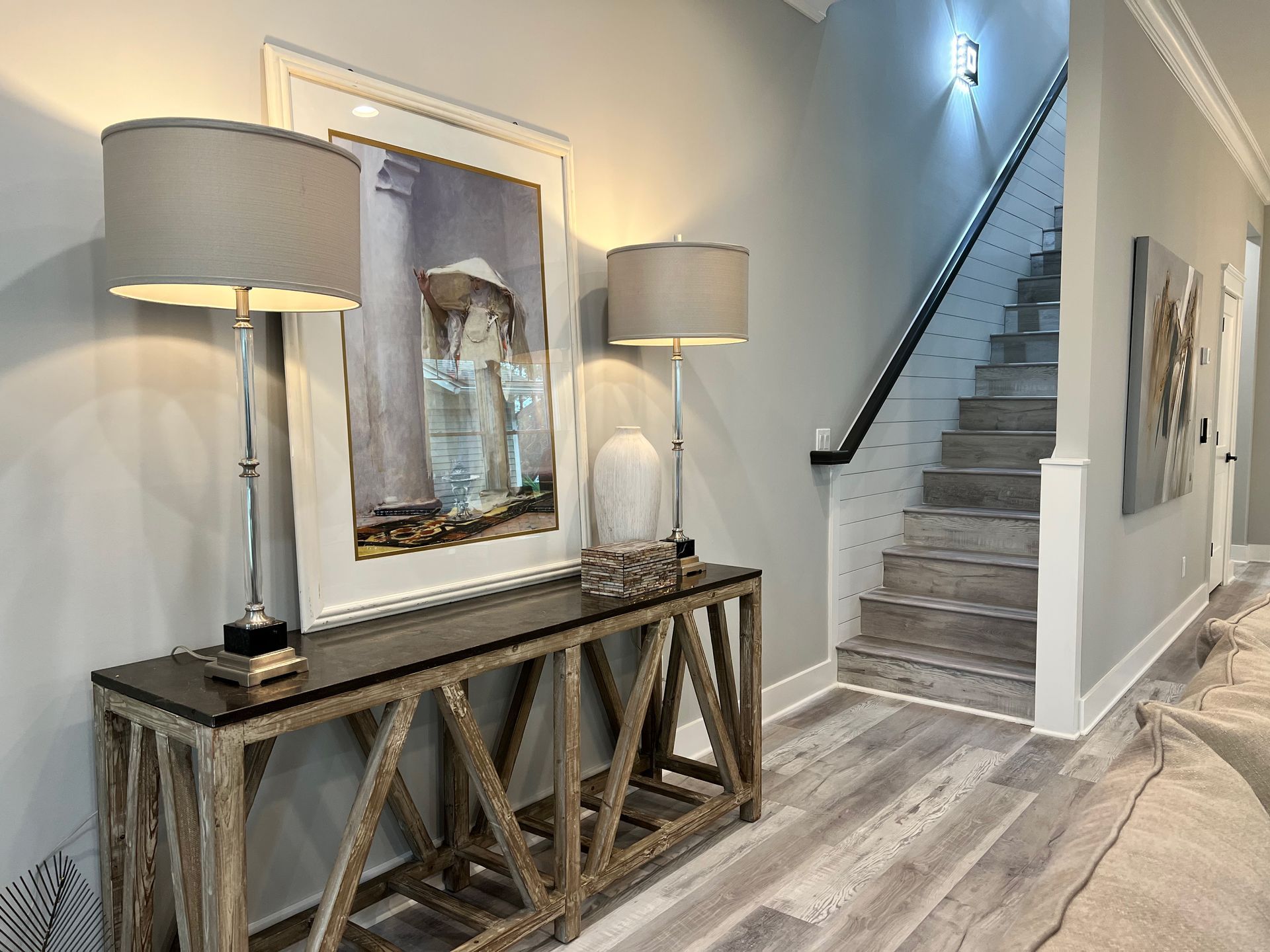 Bright hallway with a console table, lamps, mirror, and staircase in a modern home