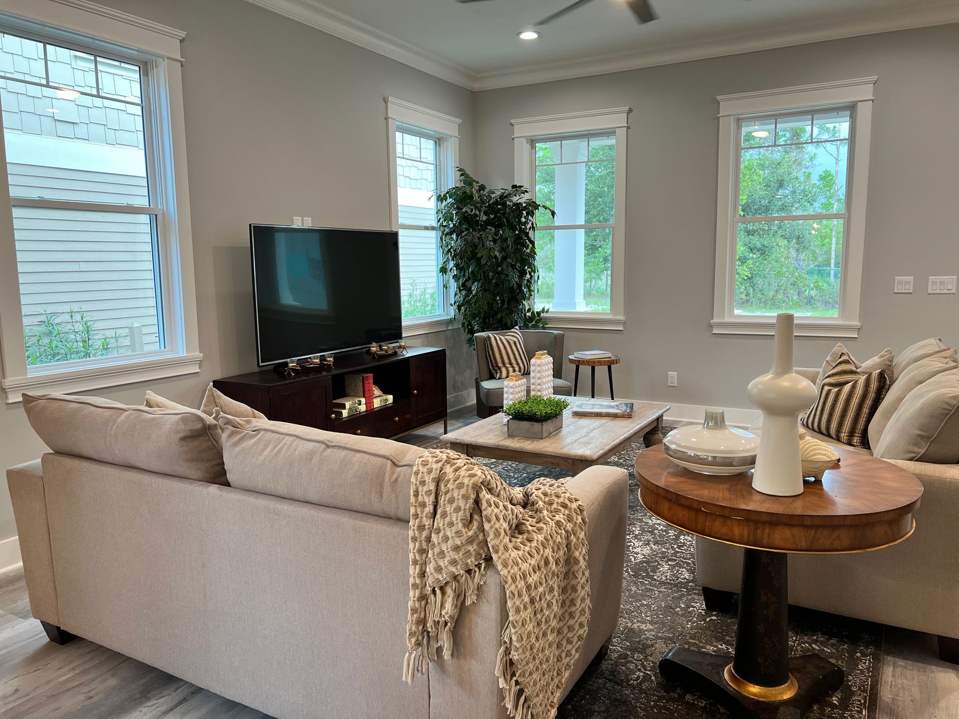 Bright living room with beige sectional, TV, coffee table, plants, and large windows