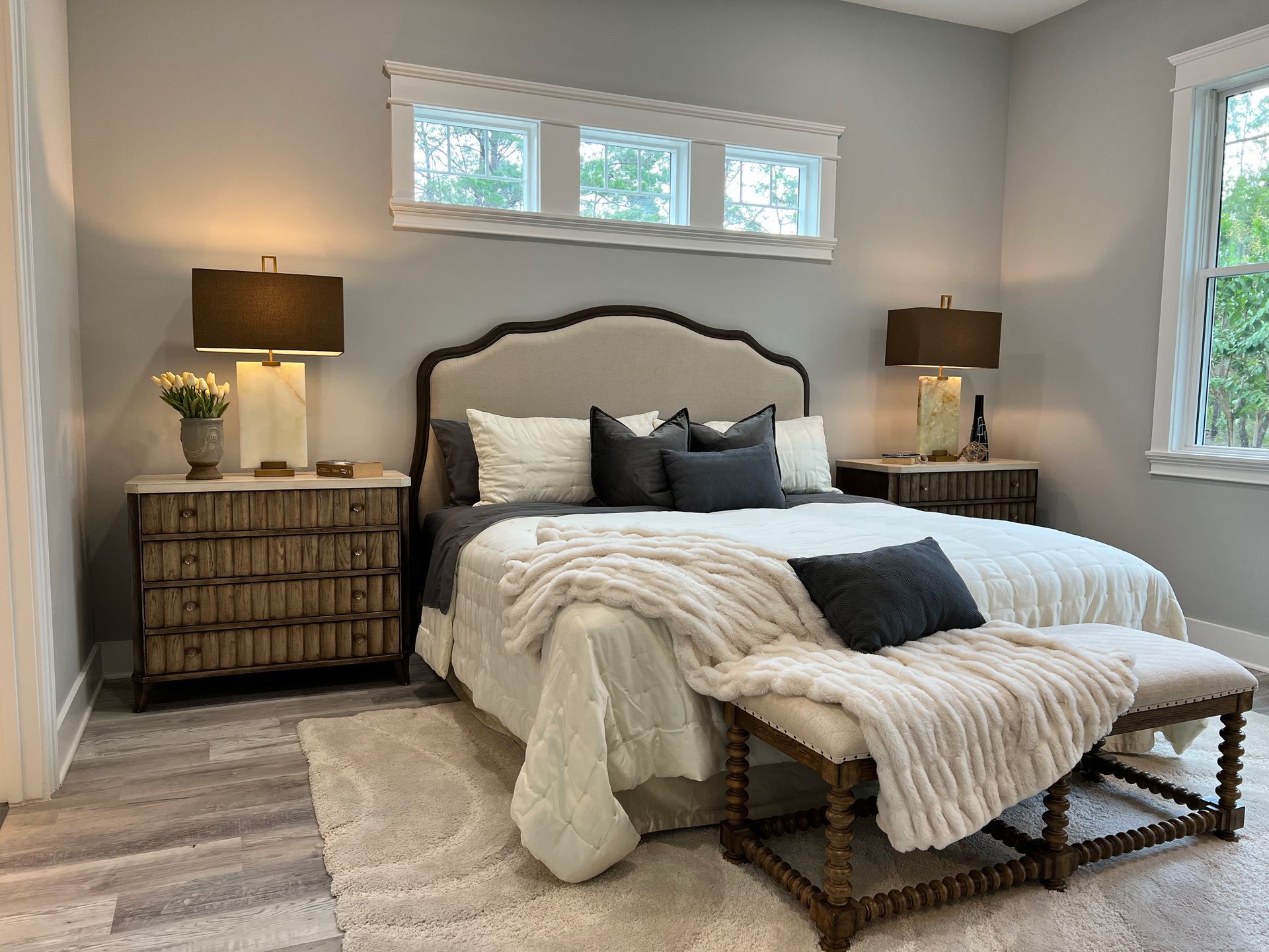 Cozy bedroom with gray walls, upholstered bed, woven nightstands, and a bench at the foot of the bed.
