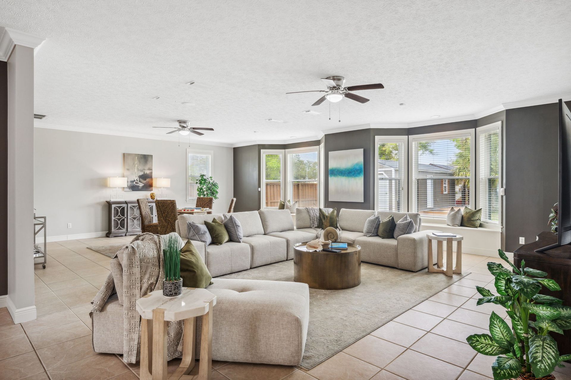 Bright living room with sectional sofa, armchairs, tiled floor, and large windows overlooking greenery