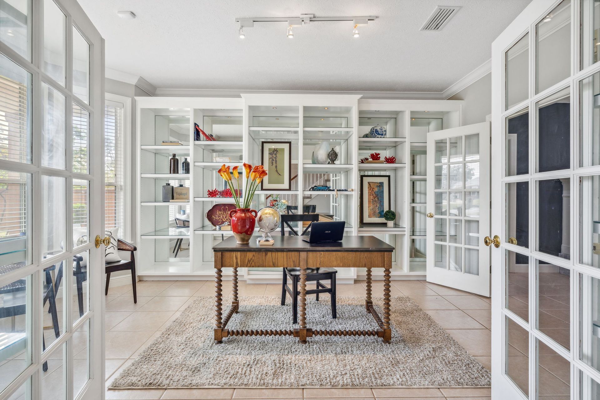 Bright home office with white built-ins, a wooden desk, and French doors, decorated with flowers.