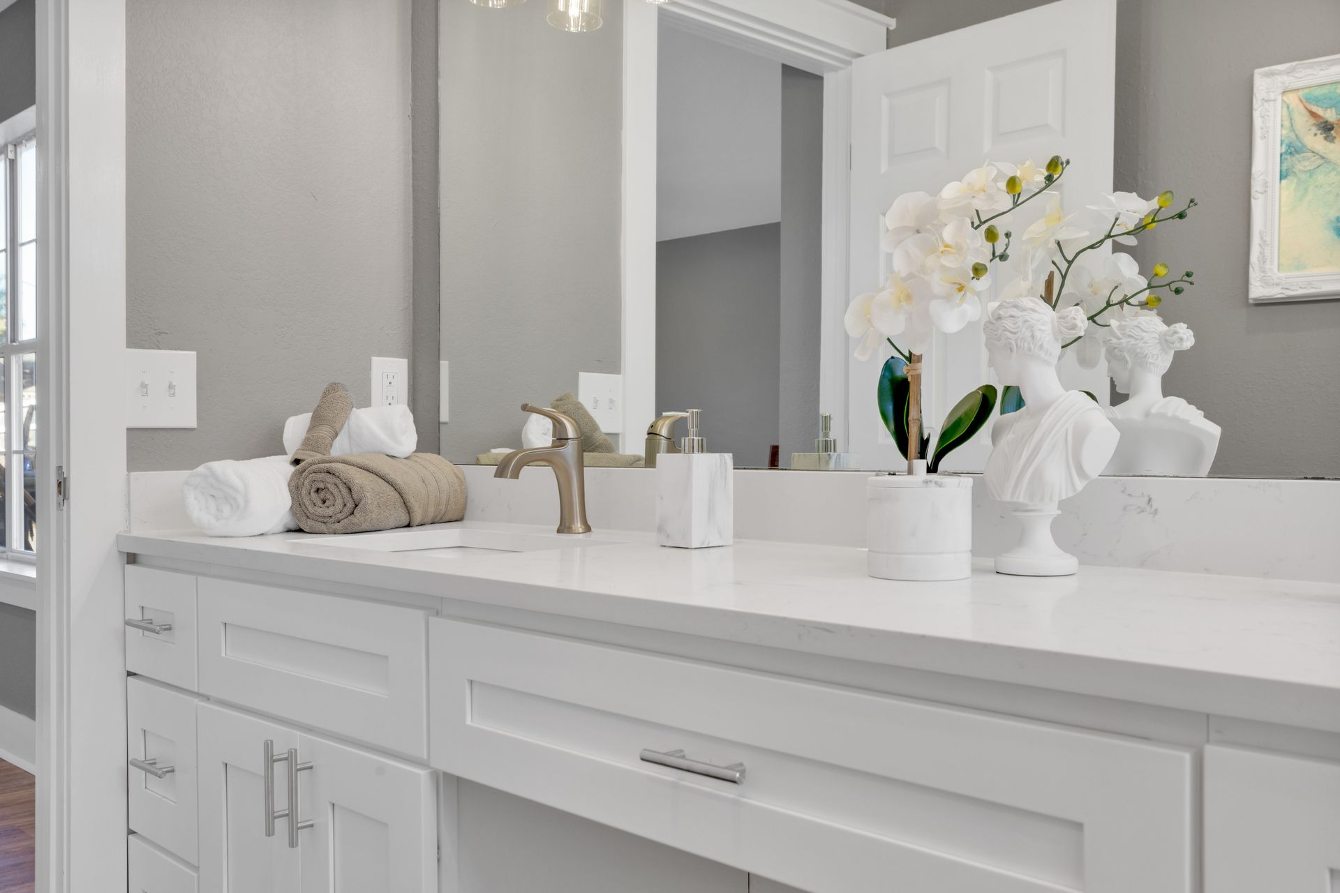 Bright bathroom vanity with white countertop, mirror, and white flowers in a vase