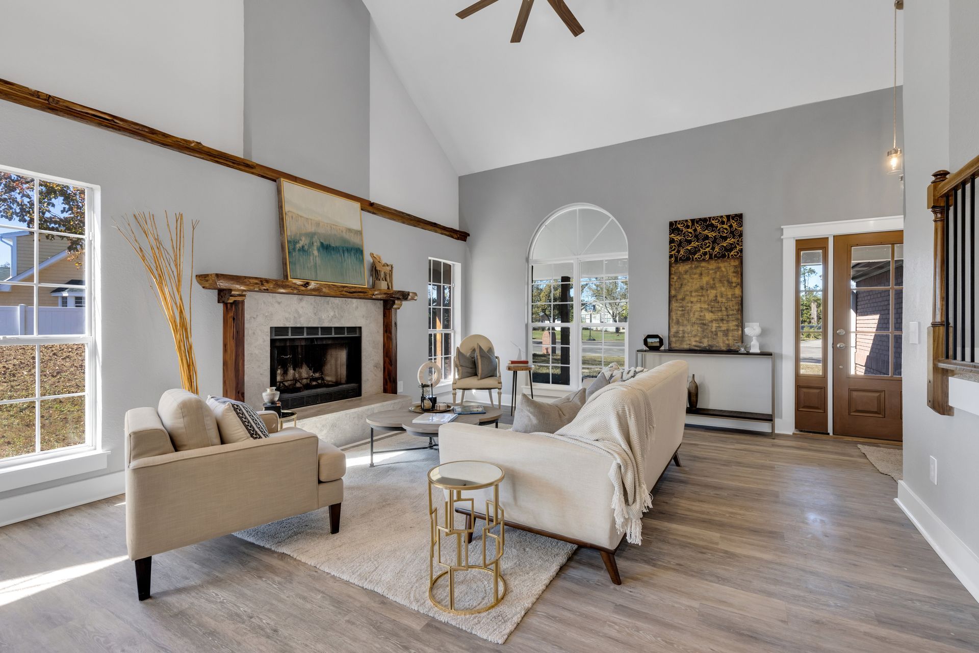 Bright living room with vaulted ceiling, fireplace, beige sofas, arched mirror, and large windows.
