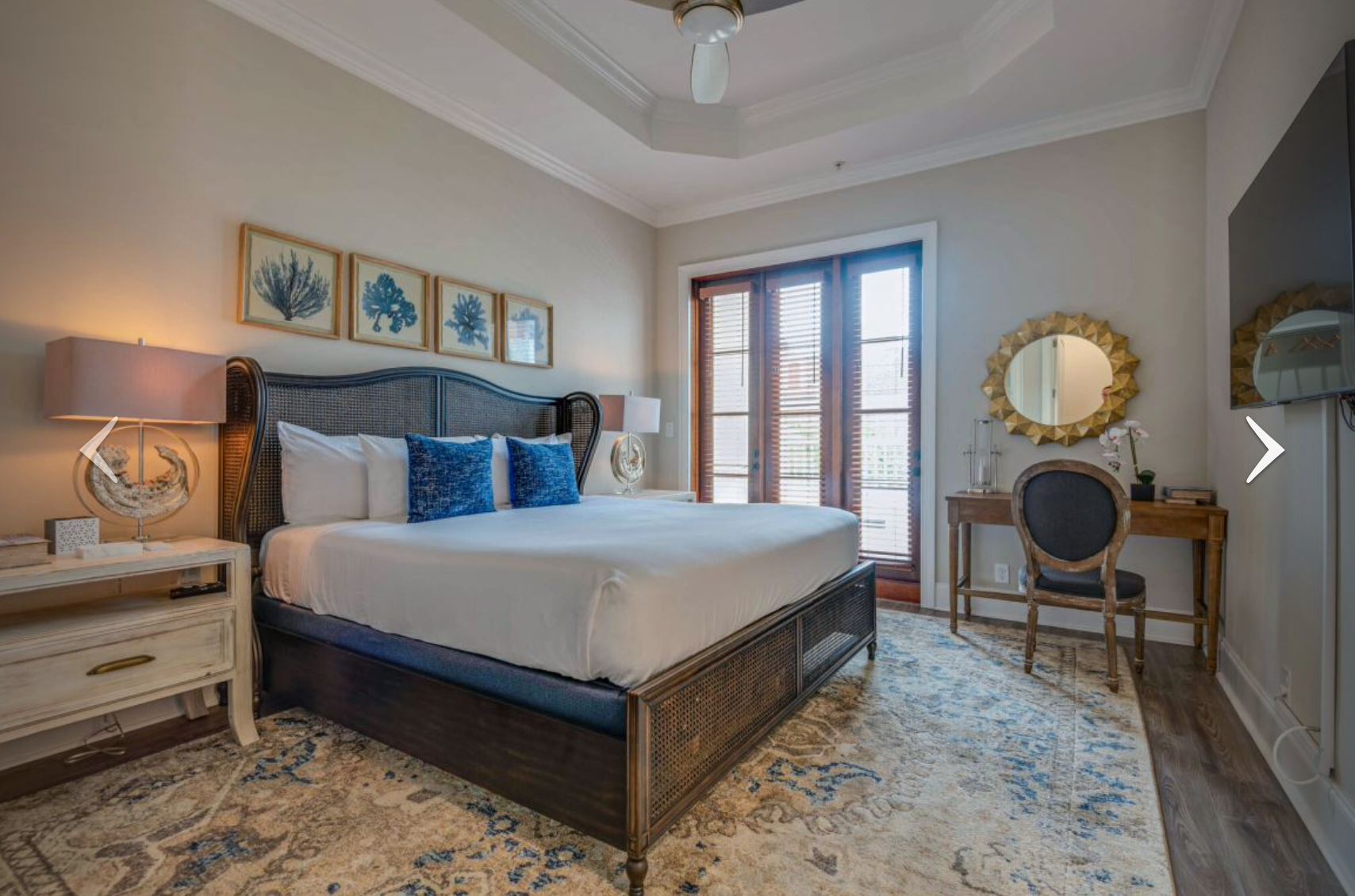 Elegant bedroom with a large bed, blue accents, vanity, and French doors opening to a balcony.