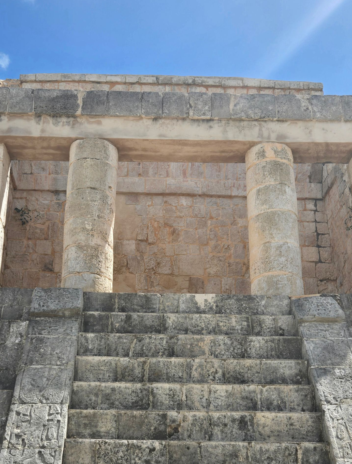 El Castillo pyramid at Chichén Itzá, a stone stepped structure under a blue sky with clouds, with visitors in the plaza.
