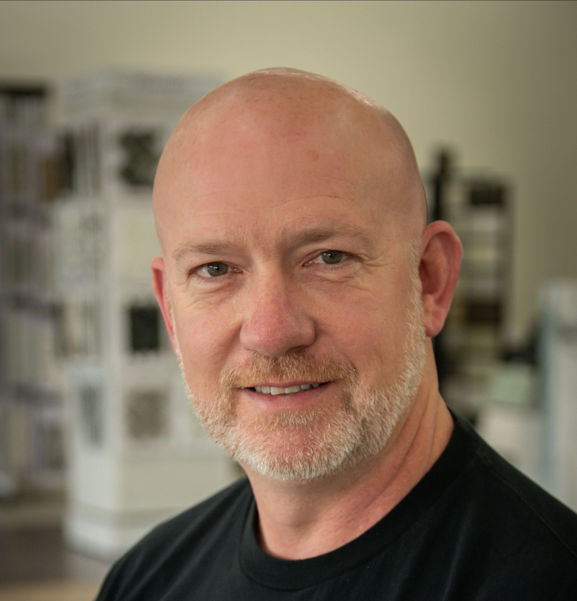 A bald man with a beard wearing a black shirt is smiling for the camera.