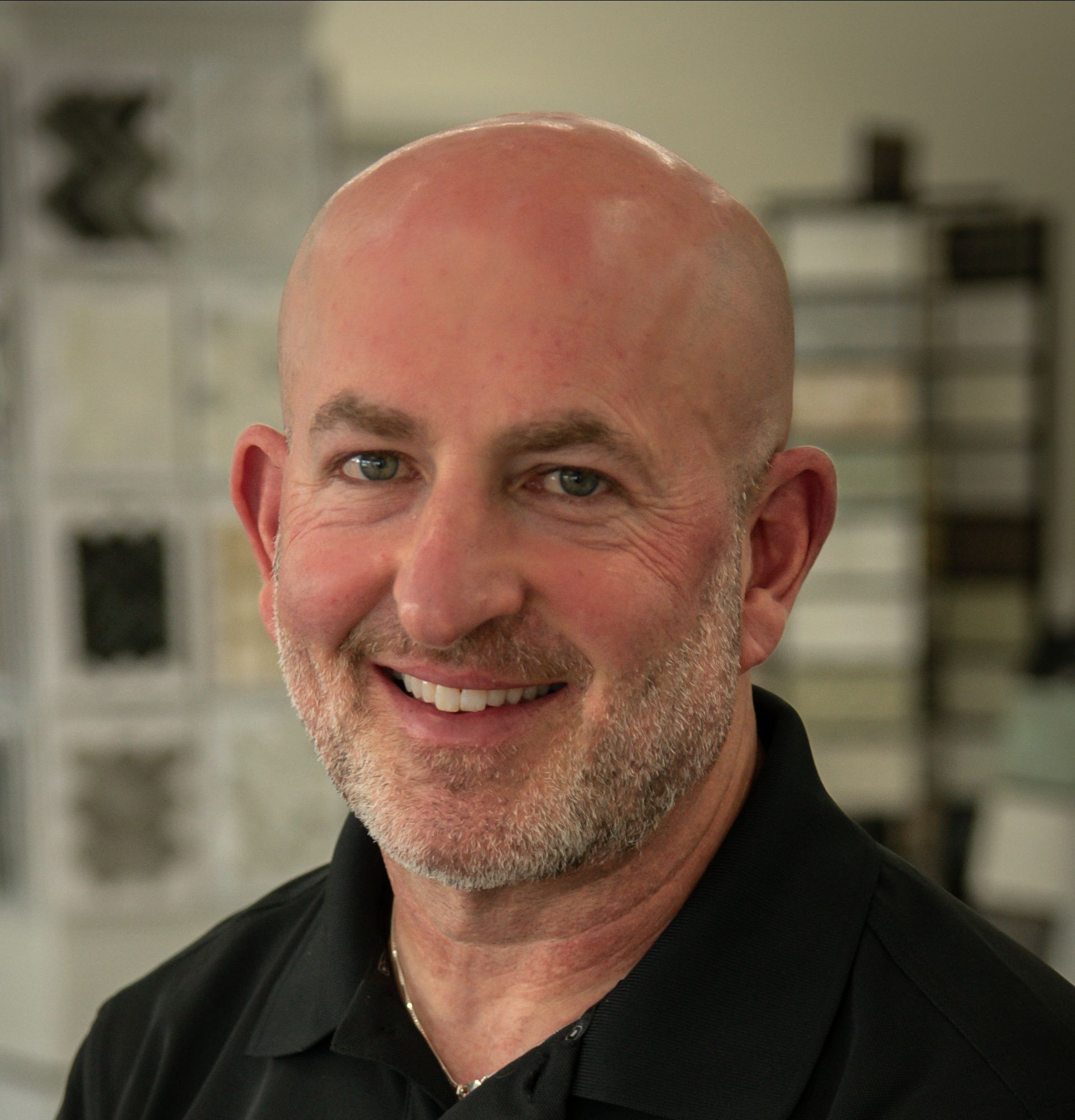 A bald man with a beard is smiling and wearing a black shirt.