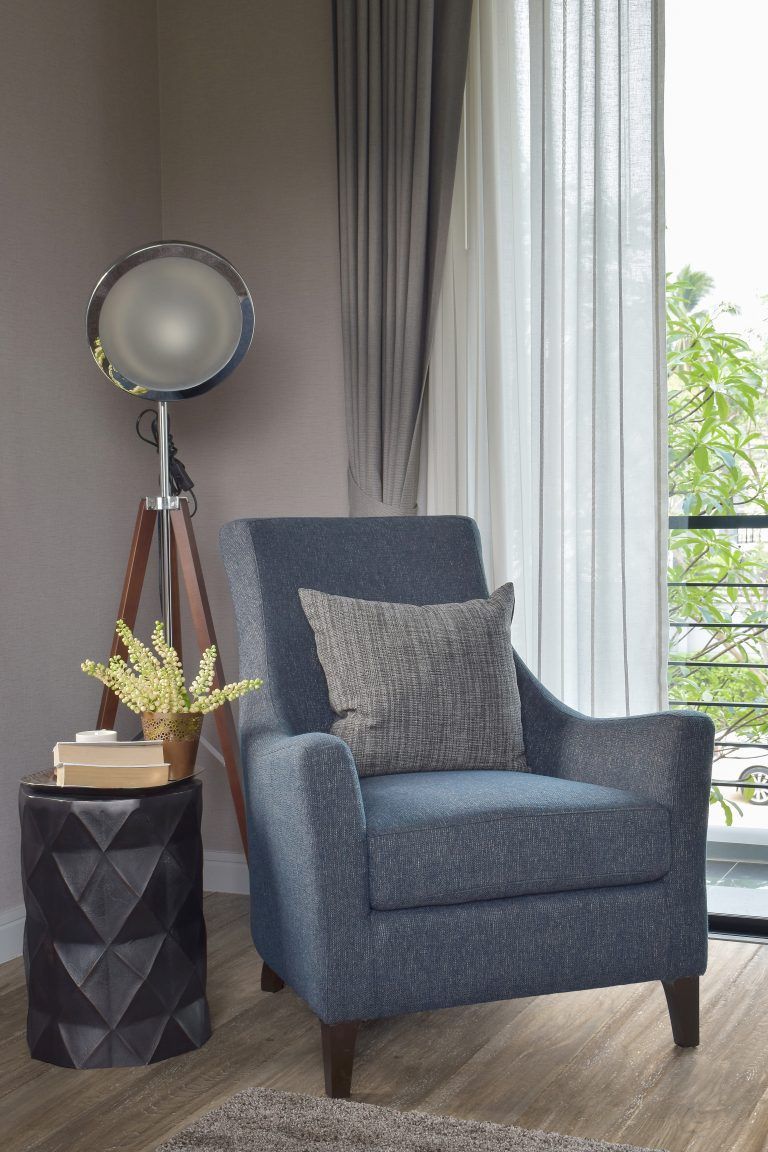 A blue chair is sitting in a living room next to a lamp.