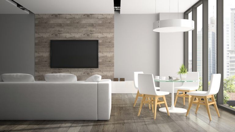 A living room with a couch , table and chairs and a flat screen tv on the wall.