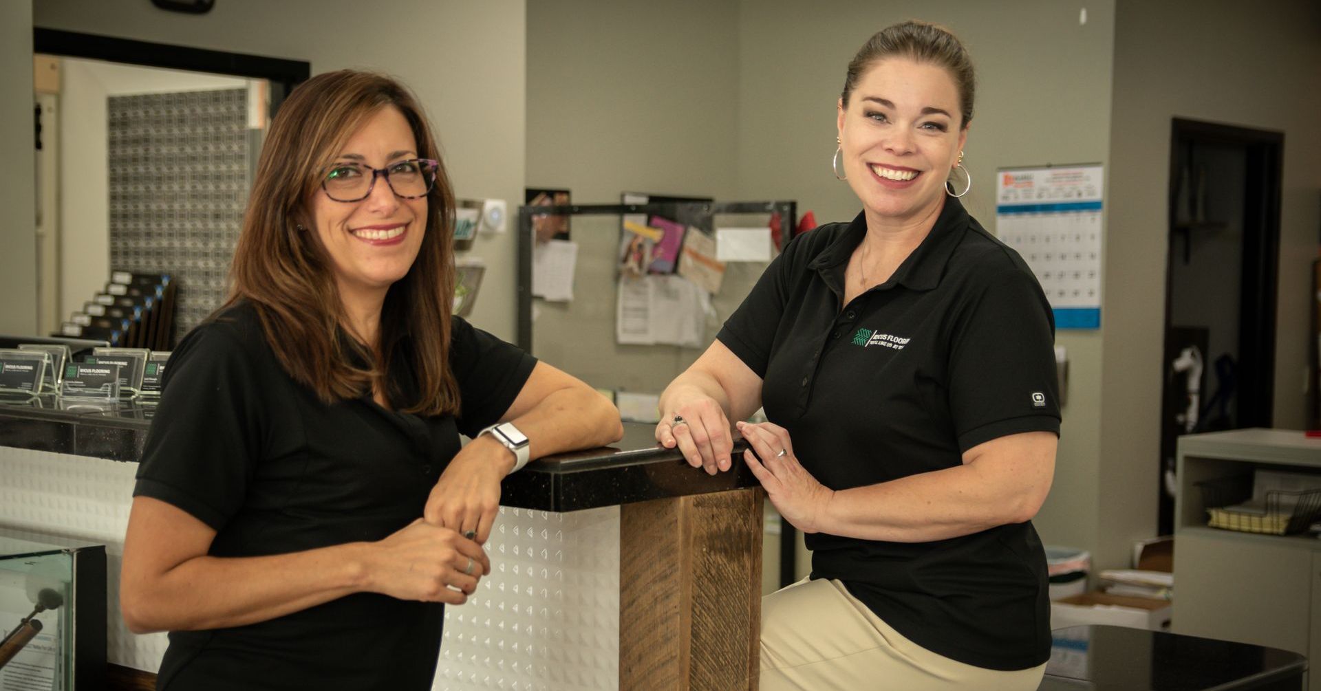 Two women are standing next to each other in an office and smiling.