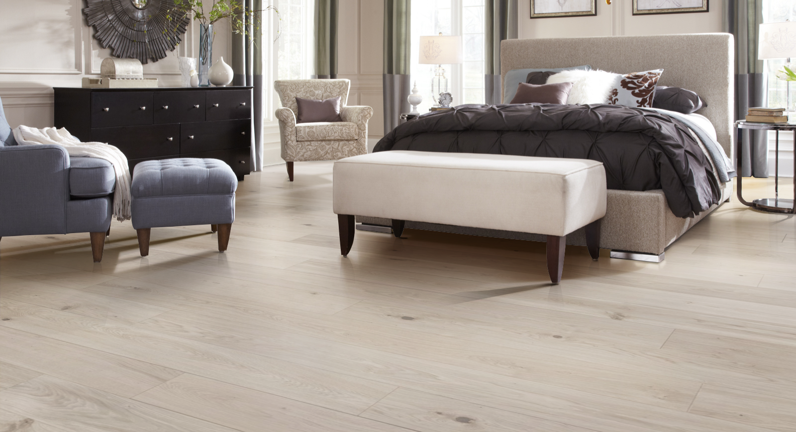 A bedroom with hardwood floors , a bed , chairs , ottomans and a dresser.