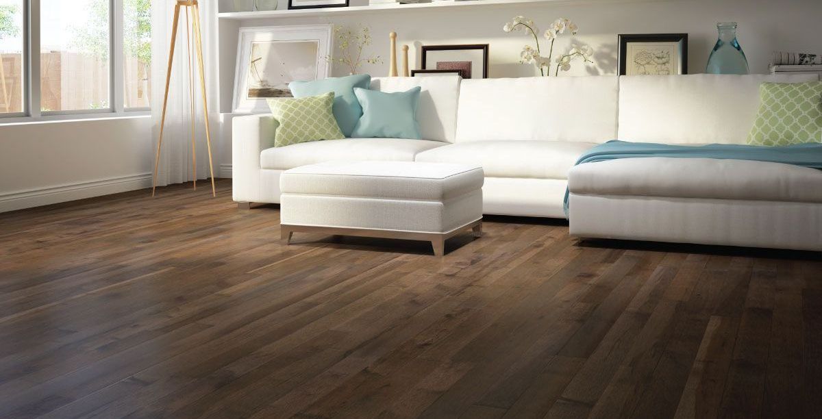 A living room with a couch , ottoman , and hardwood floor.