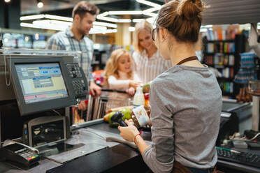A woman is sitting at a cash register in a grocery store.