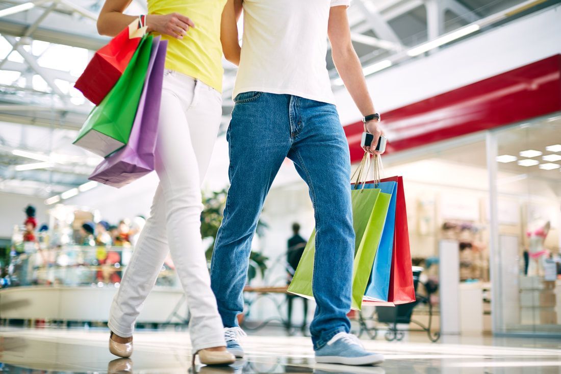 A man and a woman are walking through a mall with shopping bags.