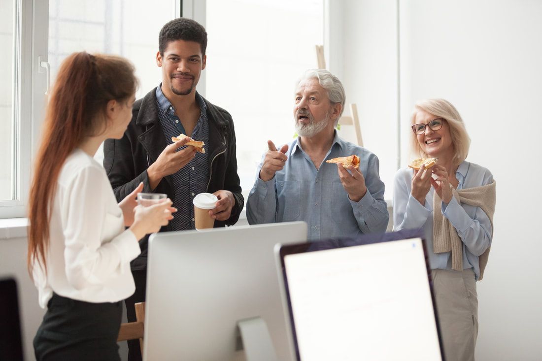A group of people are standing around a computer eating pizza.