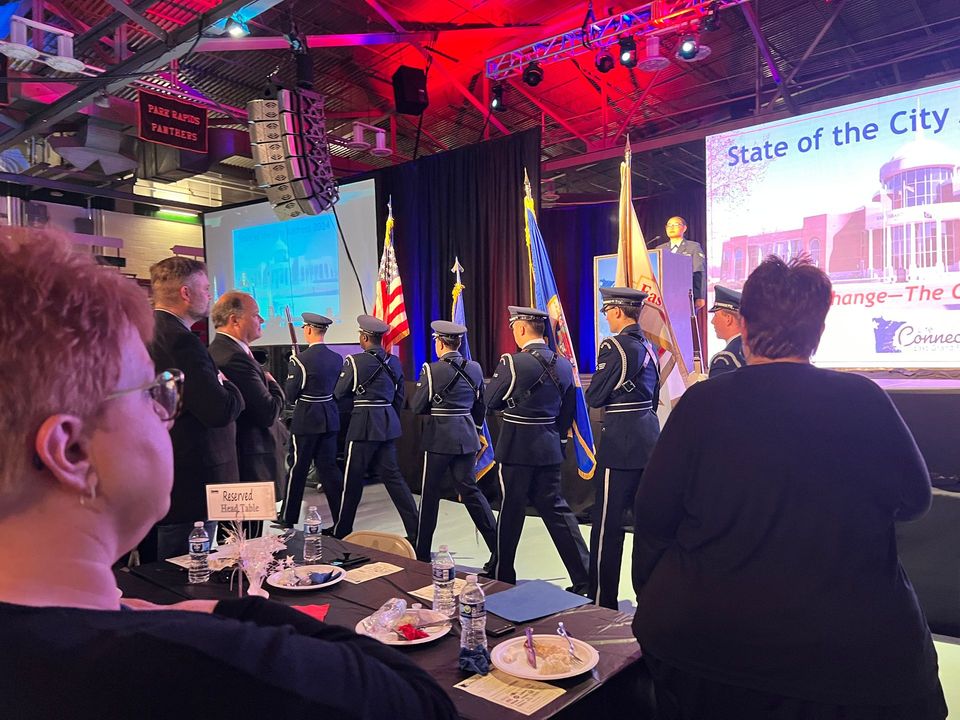 A group of people are standing in front of a stage holding flags.