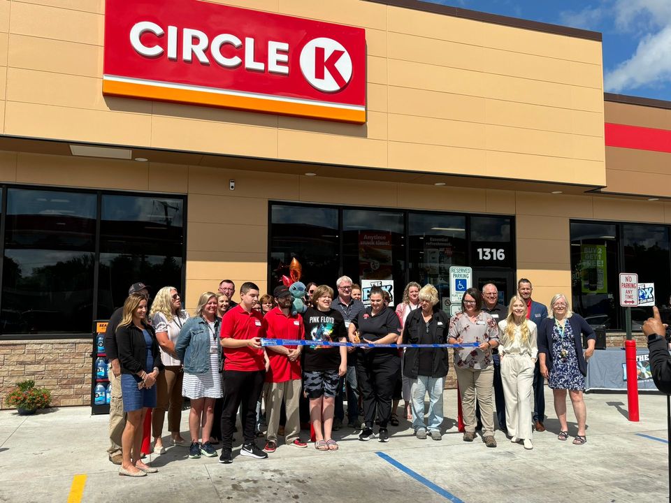 A group of people are standing in front of a circle k store cutting a ribbon.