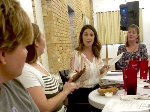 A group of women are sitting at a table talking to each other.