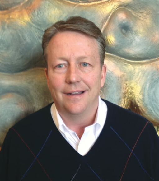 A man in a plaid sweater is smiling in front of a painting