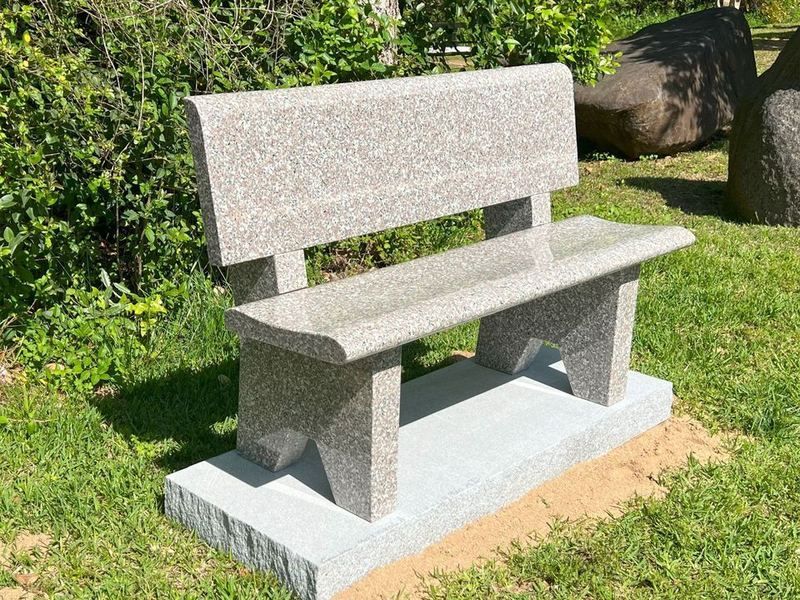 A Light Pink granite garden bench with a seat back on a gray granite base, set on a green lawn