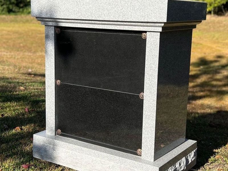 A gray granite four niche columbarium with black granite niche doors, standing on a granite base