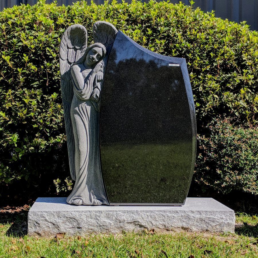 A carved standing angel beside a polished black granite upright monument