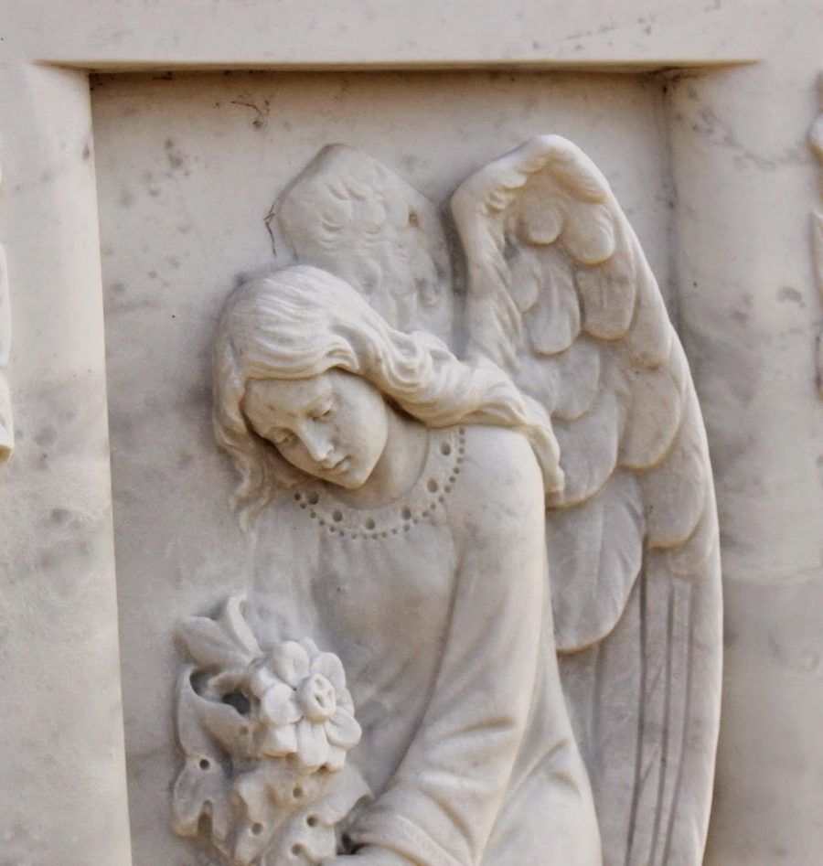 A hand carved marble angel in relief, holding flowers, on a white marble panel