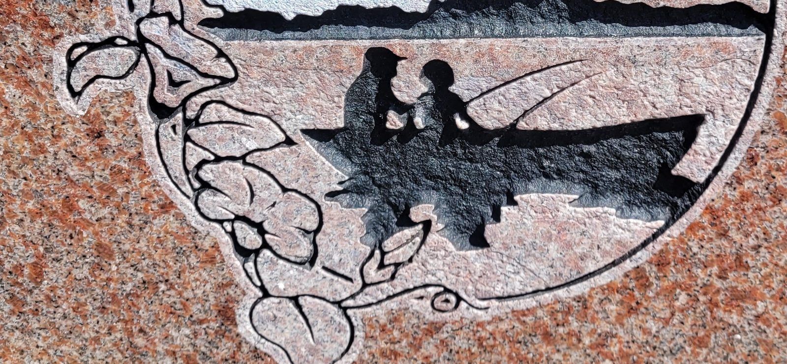 A hand etched lake scene on rose granite, two figures fishing from a boat
