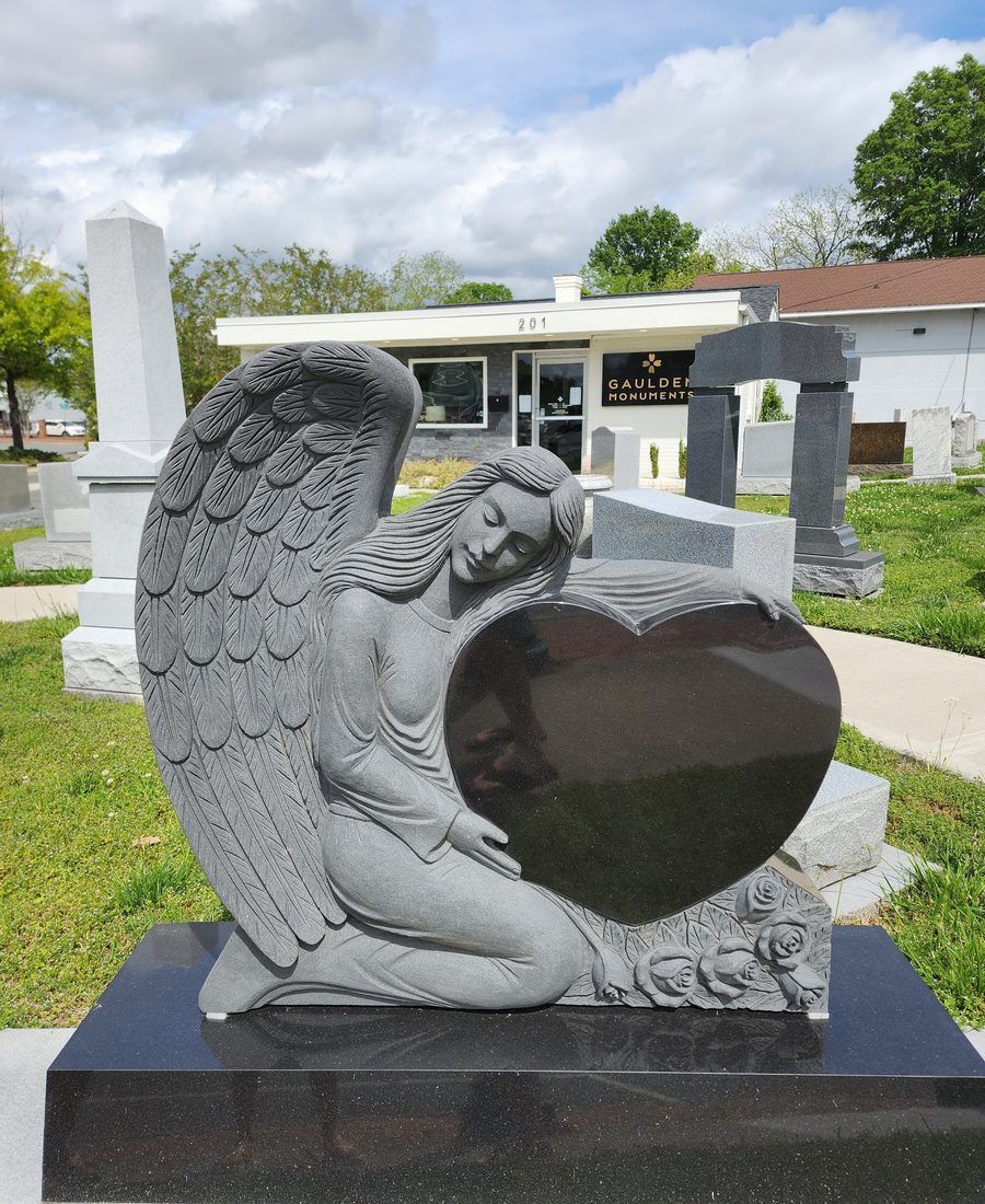 A carved kneeling angel holding a polished black granite heart, outside the Monroe showroom